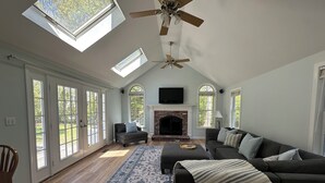 A spacious living room with a fireplace, a ceiling fan, and large windows. - Spacious 4 bedroom PRIVATE HOME
centrally located to all the Cape has to offer (Barnstable)