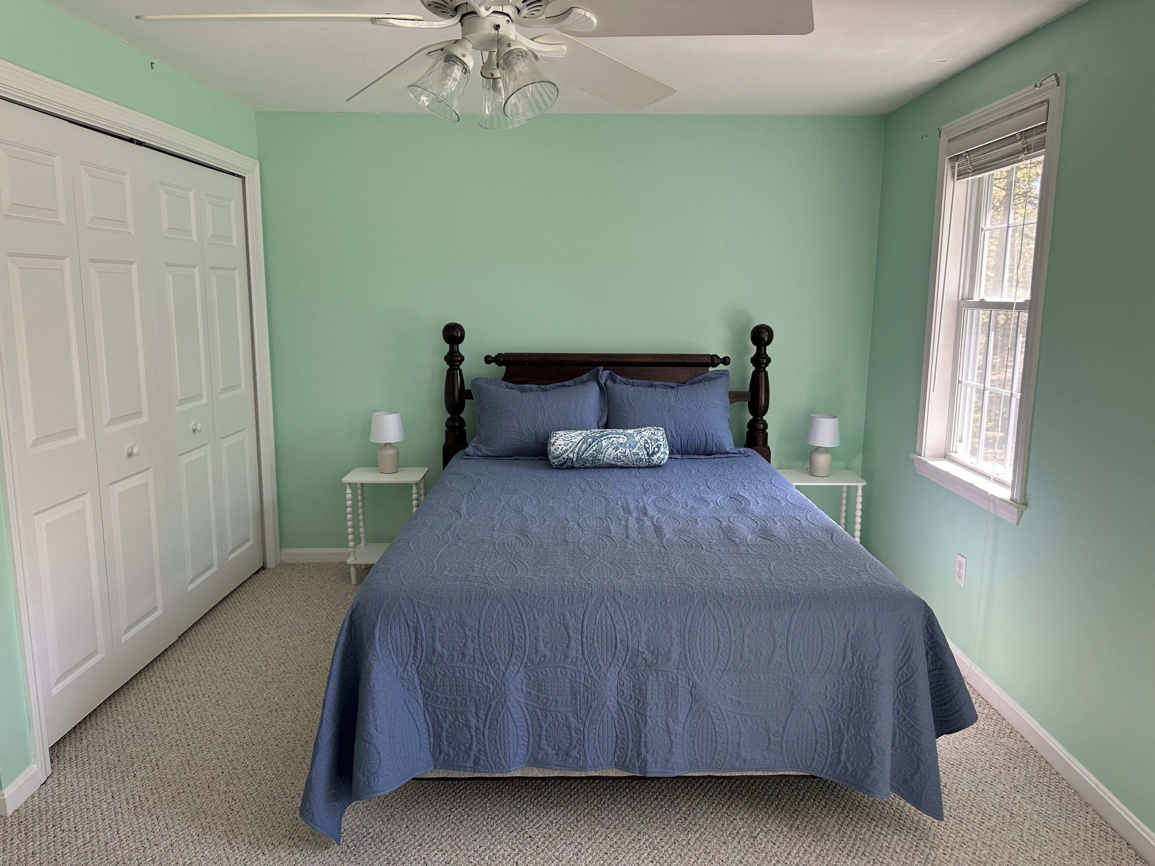 A bedroom with a bed, a ceiling fan, a window, and a door.
