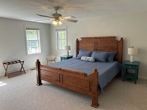Une chambre à coucher avec un lit en bois, deux tables de chevet, un ventilateur de plafond et deux fenêtres.