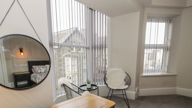 A room with a wooden desk, a chair, a round mirror, and a window with blinds. - Llety Clyd (Barmouth)