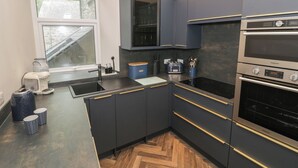 Eine moderne Küche mit dunklen Schränken, einem eingebauten Backofen und einem Fenster mit Blick auf einen Garten.
