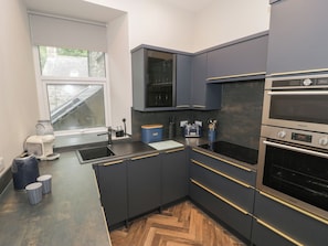 Eine moderne Küche mit dunklen Schränken, einem eingebauten Backofen und einem Fenster mit Blick auf einen Garten.
