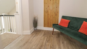 A room with a green sofa, a wooden slat wall, a white railing, and a wooden floor. - Llety Clyd (Barmouth)