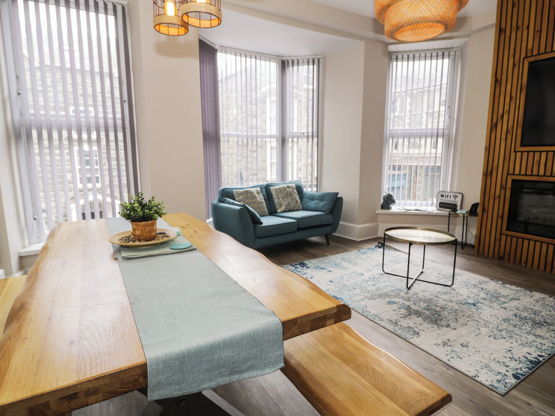 A modern living room with a wooden dining table, a blue sofa, and a small round table.