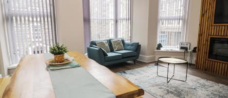 A modern living room with a wooden dining table, a blue sofa, and a small round table.