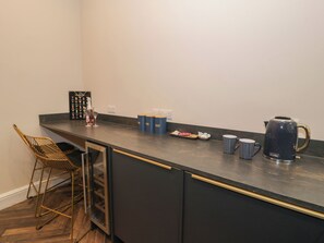 A kitchen with a bar counter, a coffee maker, and a wine glass holder. - Llety Clyd (Barmouth)