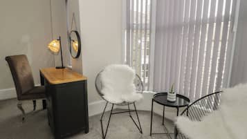 Una habitación moderna con una mesa de madera, dos sillas, una mesita redonda con una planta y un ventanal grande con persianas.