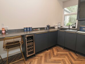 Cozinha com armários escuros, adega embutida, cafeteira e janela com vista para o verde.