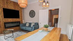 Ein Wohnzimmer mit einem TV-Schrank aus Holz, einer Couch, einem Couchtisch und einem Esstisch.