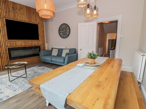 Ein Wohnzimmer mit einem TV-Schrank aus Holz, einer Couch, einem Couchtisch und einem Esstisch.