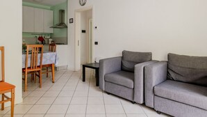 A living room with a grey sofa, a dining area with a table and chairs, and a kitchen with white cabinets and a red kettle. - GuestHost - Seaside Sanctuary with balcony and parking (Rimini)