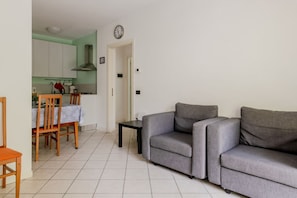 A living room with a grey sofa, a dining area with a table and chairs, and a kitchen with white cabinets and a red kettle. - GuestHost - Seaside Sanctuary with balcony and parking (Rimini)