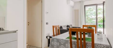 A dining area with a table set for two, a sofa, and a window with curtains.