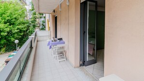 A balcony with a table and chairs, a sliding door, and a view of greenery. - GuestHost - Seaside Sanctuary with balcony and parking (Rimini)