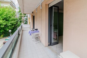 A balcony with a table and chairs, a sliding door, and a view of greenery. - GuestHost - Seaside Sanctuary with balcony and parking (Rimini)