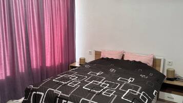 Un dormitorio con cama, cortinas, una mesita de noche y un equipo de aire acondicionado.