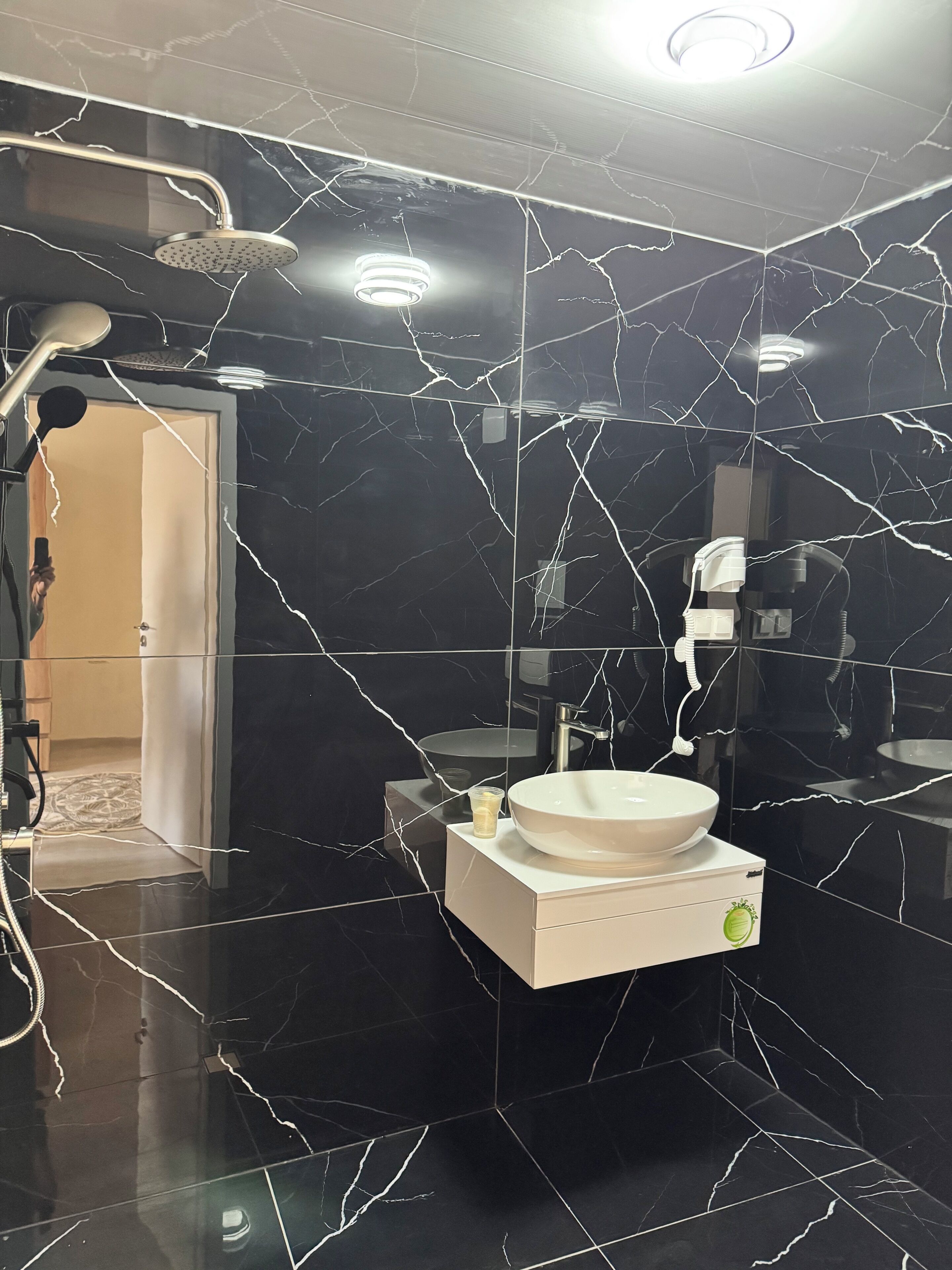 Une salle de bain avec un sol en marbre noir, un lavabo blanc et une douche.