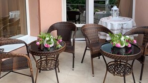 Un patio con mobiliario de mimbre, una mesa redonda y una puerta de vidrio que da a un espacio al aire libre.