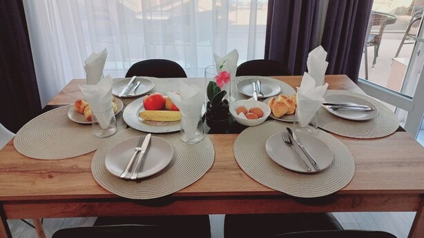 Mesa de comedor dispuesta con platos, cubiertos y una frutera, con vistas al exterior a través de amplias ventanas.