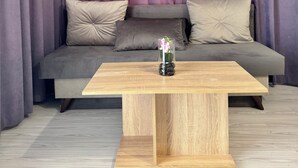 Un salón moderno con un sofá gris, dos cojines color beige y una mesa de centro de madera con un jarrón de cristal con flores.