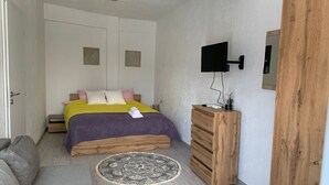 Un dormitorio con cama, cómoda de madera, televisor y alfombra estampada.