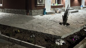 Un edificio con unidades de aire acondicionado, entrada empaveda de piedra y un pequeño jardín.