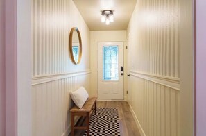 A hallway with a checkered floor, a bench, a mirror, and a door with a window.