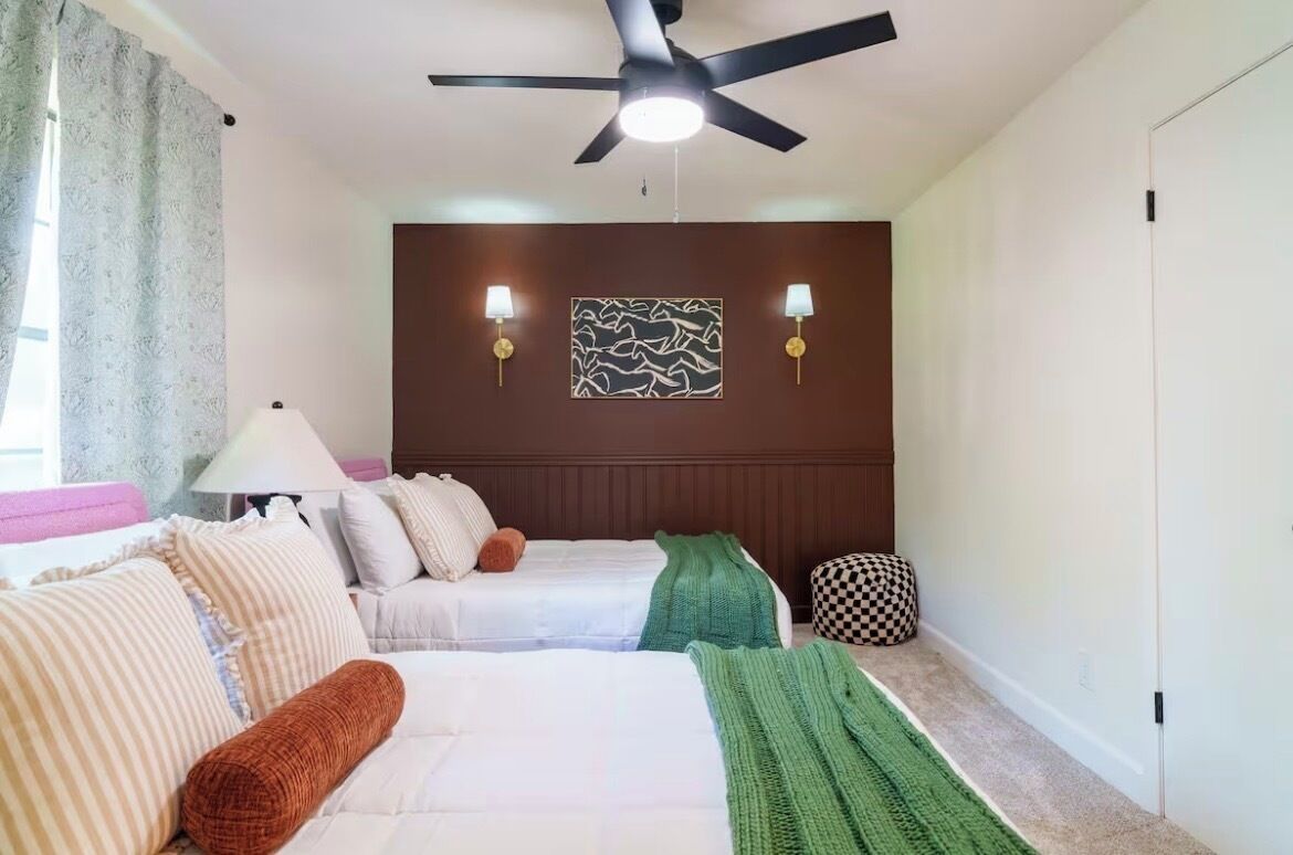 A hotel room with two beds, a ceiling fan, wall-mounted lamps, and a patterned wall decoration.