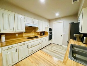 Eine Küche mit weißen Schränken, einer Holz Arbeitsplatte, einem Spülbecken, einem Backofen und einem Kühlschrank.