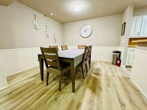 Ein Esszimmer mit einem rechteckigen Tisch, sechs Stühlen, einer Wanduhr und einem Mülleimer.