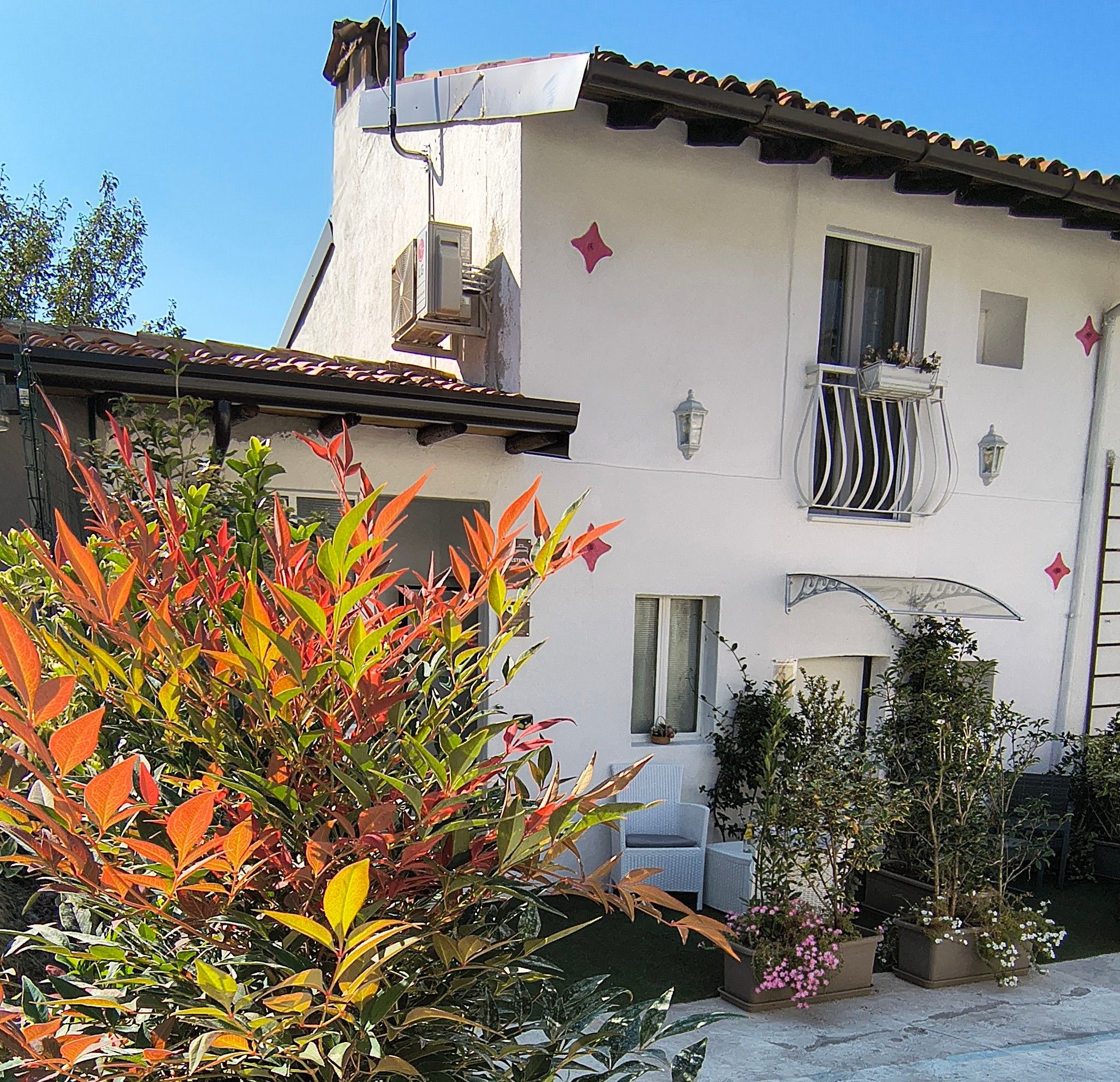 A two-story building with a balcony, a window with a decorative awning, and a small garden area with various plants.