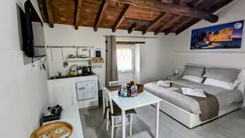 A compact hotel room with a kitchenette, a bed, a dining table, and a painting of a castle.