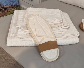 A neatly folded white towel and a pair of white slippers with a brown strap on a table.