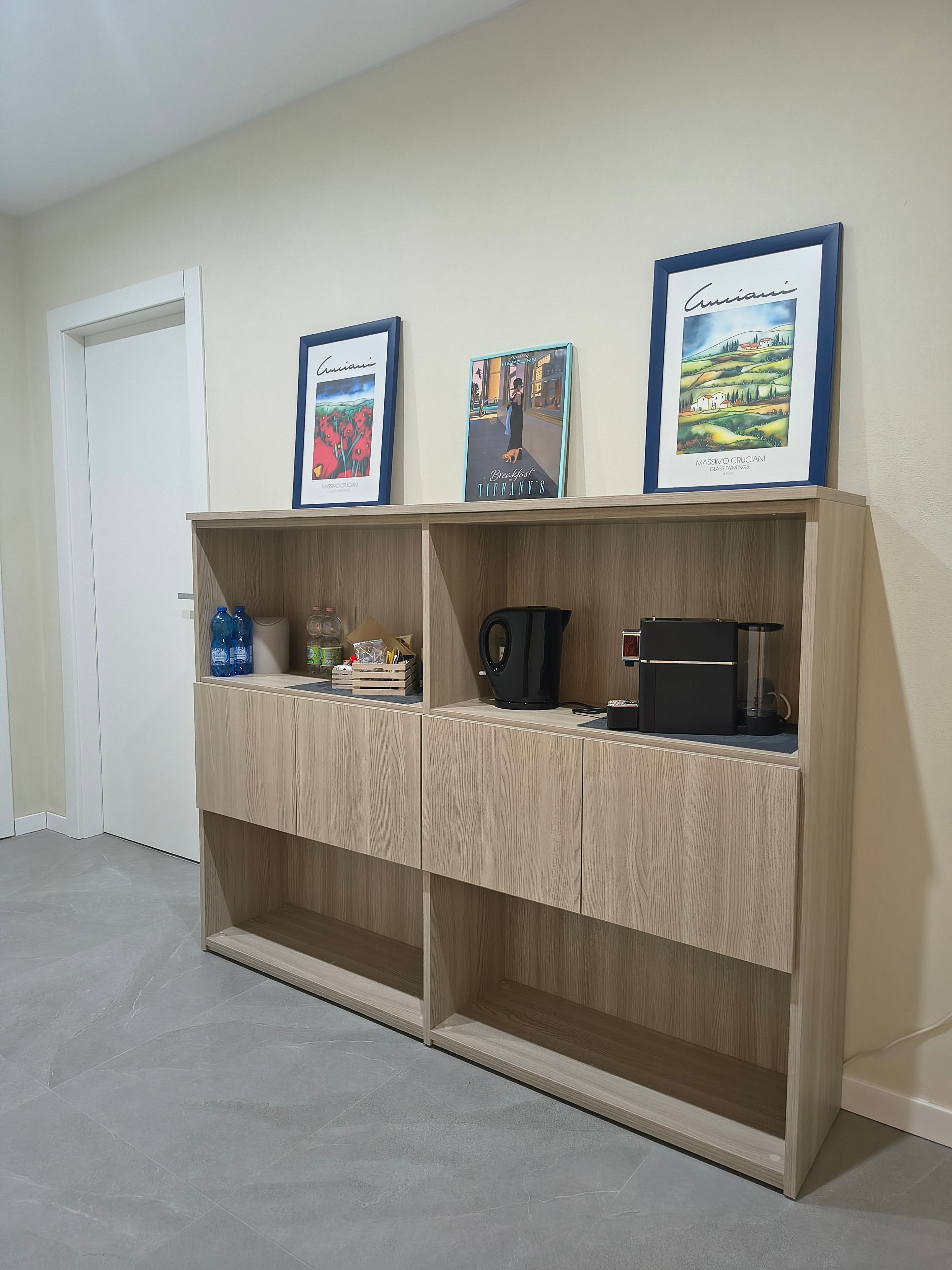 Una stanza con un'unità contenitore in legno addossata a una parete, che ospita opere d'arte incorniciate, una macchina da caffè e un bollitore.