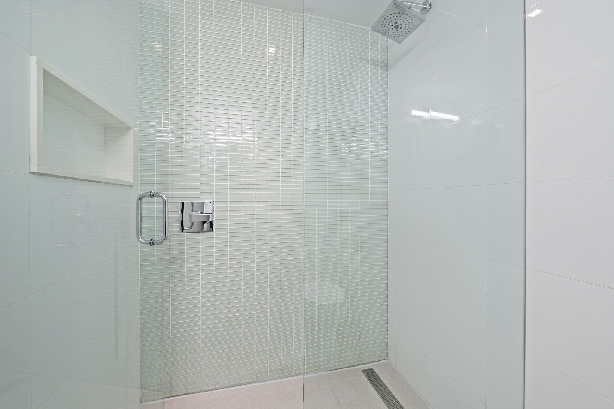 A glass-enclosed shower with a frosted glass door, a metal handle, and a showerhead.