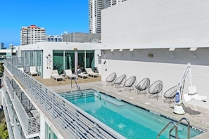 A rooftop pool with lounge chairs and a glass-enclosed area. - 6080 Collins  (Miami Beach)