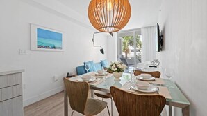 A dining area with a glass table, wooden chairs, a hanging light fixture, and a painting on the wall. - 6080 Collins  (Miami Beach)