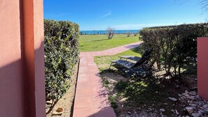 Un sentier qui mène à une zone herbeuse offrant une vue sur la mer, un bosquet et un ciel bleu dégagé.