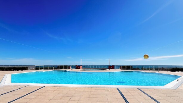Une piscine extérieure rectangulaire à l’eau d’un bleu limpide, entourée d’une terrasse carrelée.