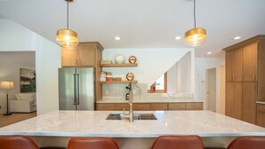 Une cuisine moderne dotée d’un grand îlot central, d’appareils électroménagers en acier inoxydable, de meubles en bois et de luminaires suspendus.