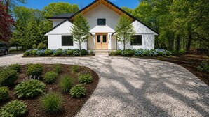Une maison moderne à deux étages, dotée d’une façade symétrique, d’une entrée centrale et d’une allée gravillonnée.