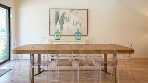 Un coin repas avec une table en bois et des chaises transparentes, un tableau accroché au mur et deux vases posés sur un meuble.