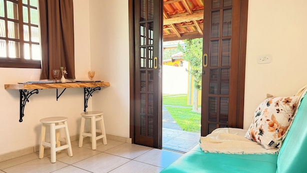 A room with a teal sofa, a wooden table with stools, and a door leading to an outdoor area. - Chalés Caminho das Pedras S. B. Sapucaí (São Bento do Sapucaí)