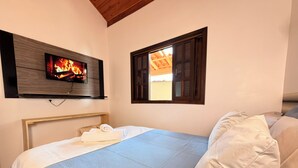 A bedroom with a bed, a TV mounted on the wall, and a window. - Chalés Caminho das Pedras S. B. Sapucaí (São Bento do Sapucaí)