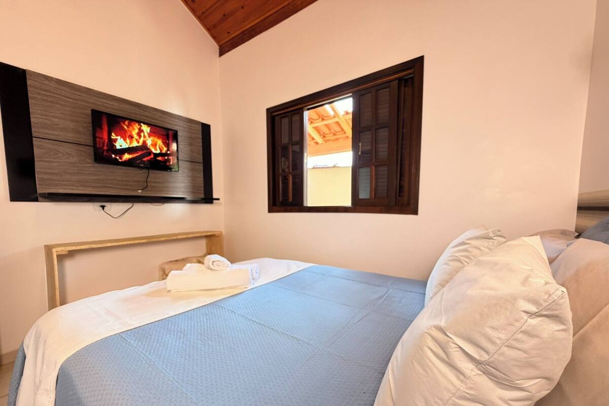 Ein Schlafzimmer mit Bett, einem an der Wand befestigten Fernseher und einem Fenster.