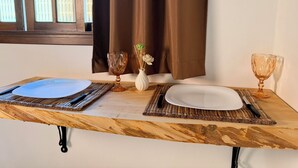 A dining table with placemats, plates, cutlery, and glassware, set against a window with curtains. - Chalés Caminho das Pedras S. B. Sapucaí (São Bento do Sapucaí)