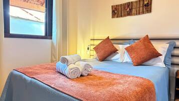 Une chambre d’hôtel avec un lit, des oreillers, une couverture et une fenêtre donnant sur des immeubles.