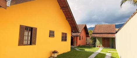 A yellow building with a sloped roof, a small garden area with a pathway, and a mountain in the background.