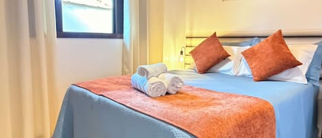 A hotel room with two beds, a window, a wall-mounted artwork, and a neatly made bed with towels.