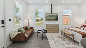 Une chambre moderne avec un canapé en cuir marron, une table basse ronde, un lit recouvert d’une couvre-lit à motifs et un tableau accroché au mur.
